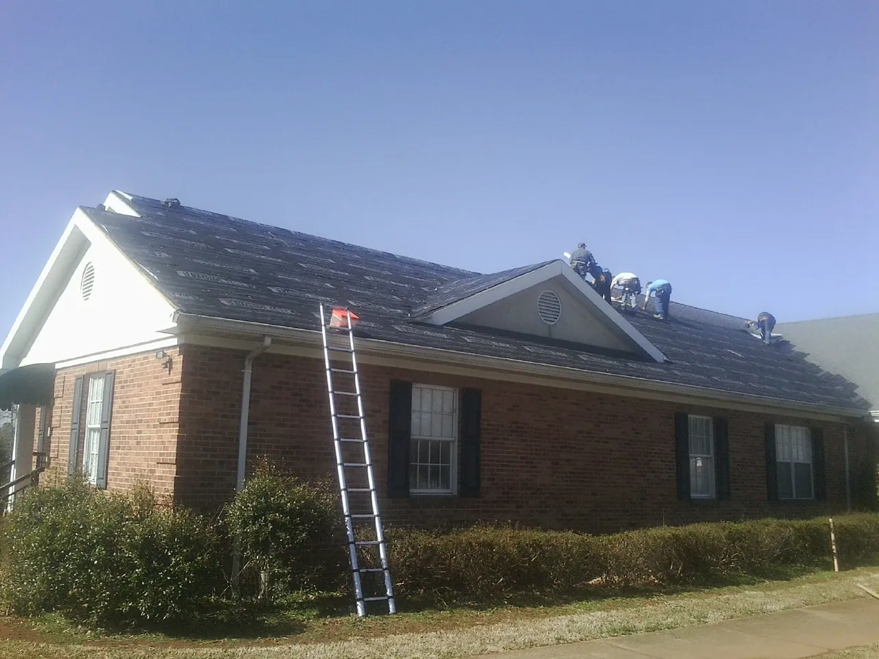 Crew tearing shingles off a brick ranch roof with a ladder set — Metal Roof Repair work by our crew in Belle Vernon