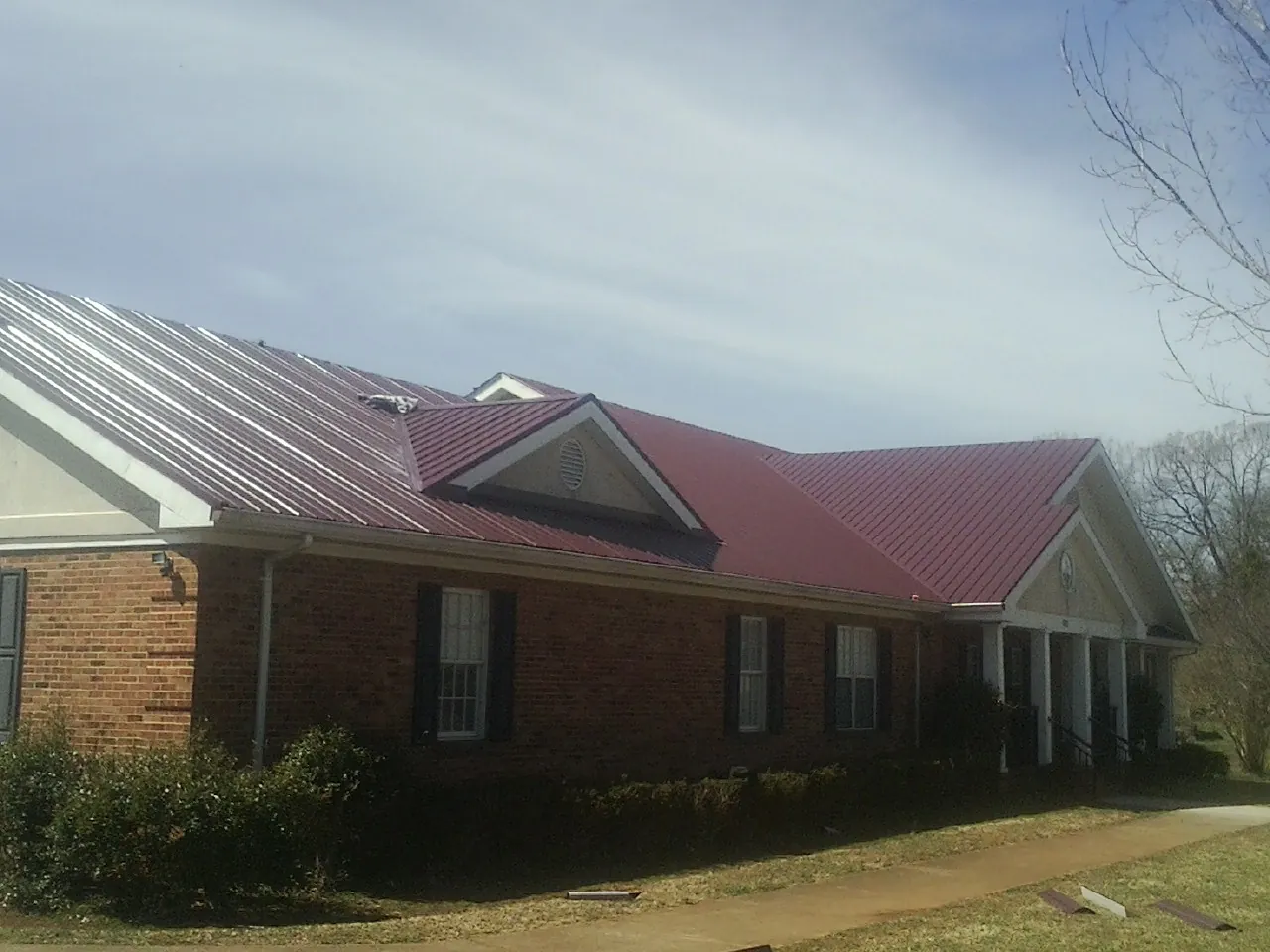 Red metal roof with gabled entries on a long brick building, from a Hail Damage Roof Repair job in Belle Vernon