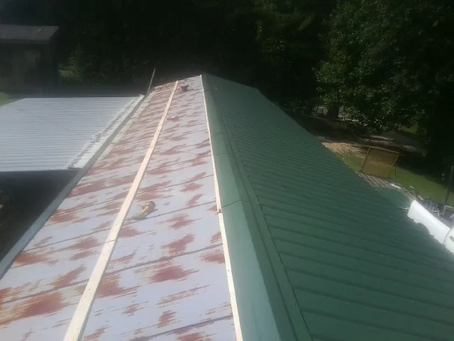 Old rusted panels beside newly installed green metal roofing — Wind Damage Roof Repair by Roofing Brothers in Belle Vernon