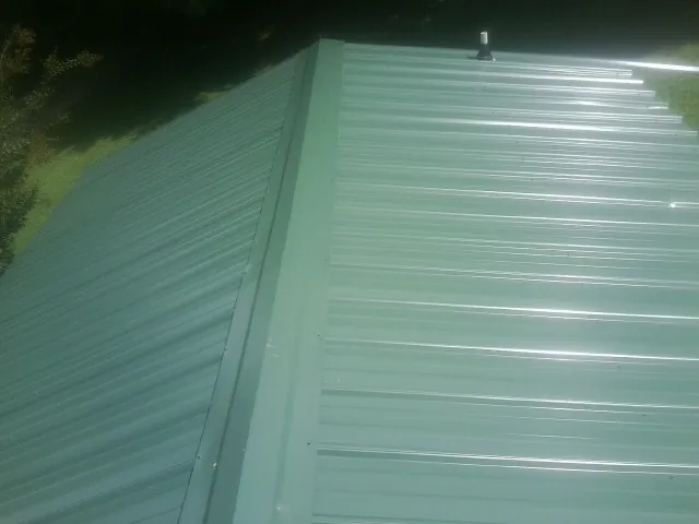 New green metal panels meeting at the ridge of a roof — Flat Roof Repair work by our crew in Belle Vernon