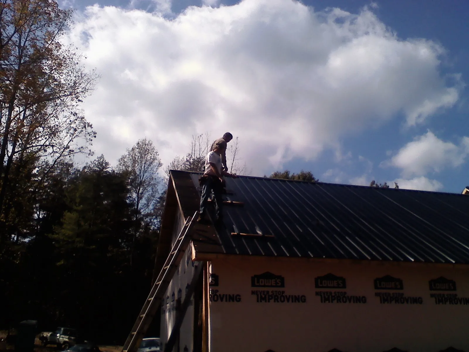 Roofer fastening dark metal panels high against a cloudy sky, from a Roof Inspection job in Belle Vernon