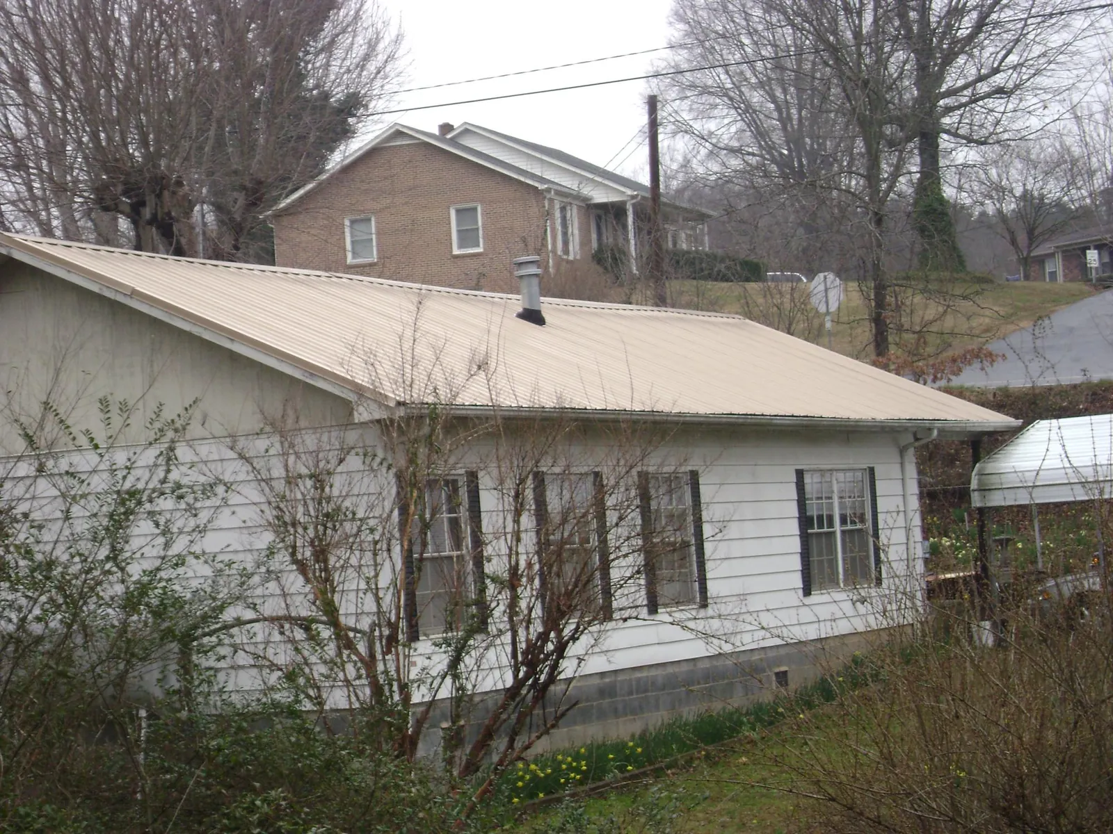 Tan metal roof on a white sided house set into a hillside — Commercial Roofing by Roofing Brothers in Belle Vernon