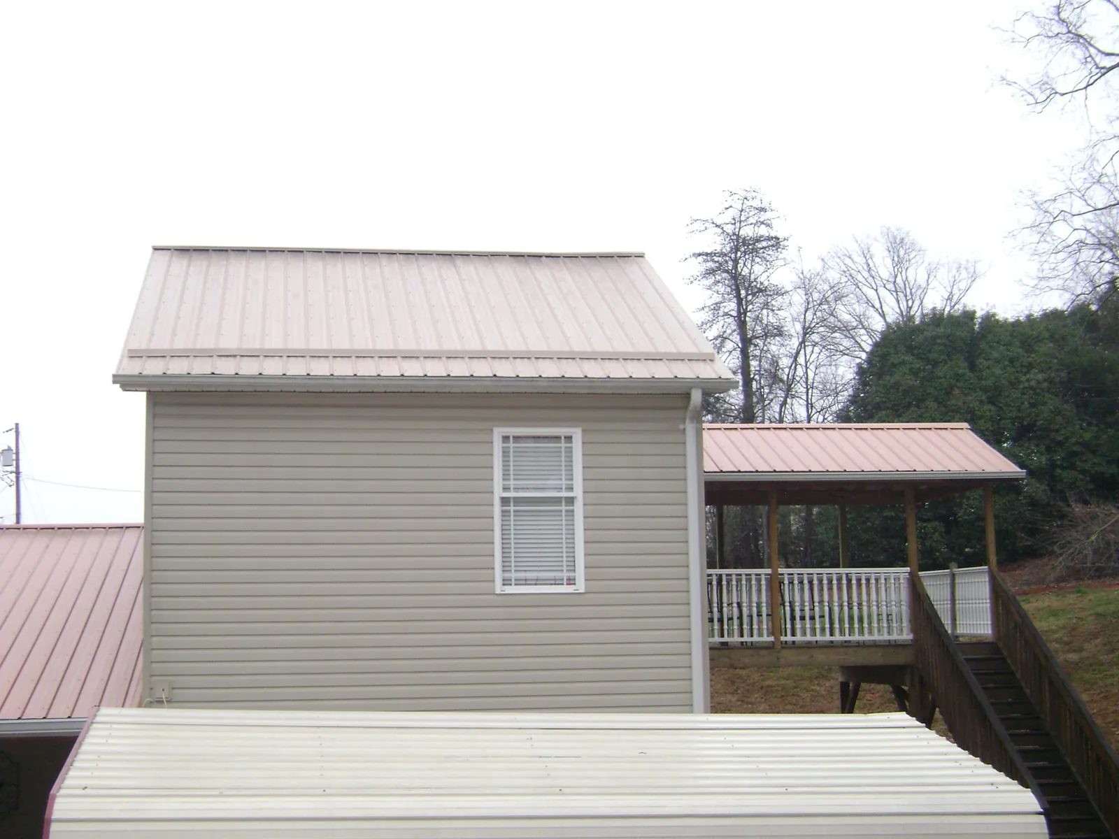 Tan metal roofs on a two story addition and attached porch, from a Roof Replacement job in Belle Vernon